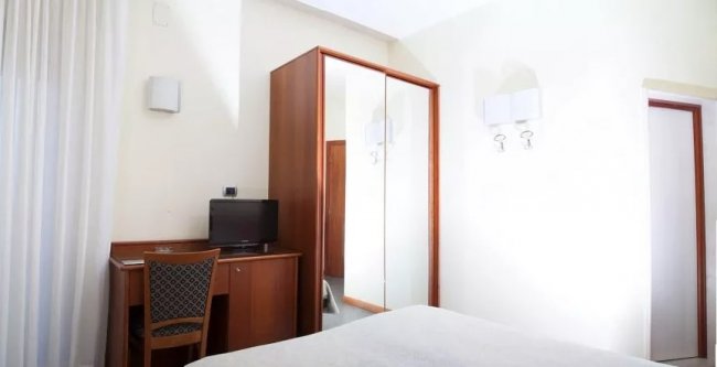 Camera d'albergo con armadio a specchio, scrivania, sedia e TV.