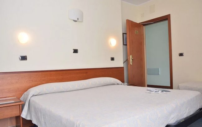 Camera con letto matrimoniale, due applique accese e porta aperta.
