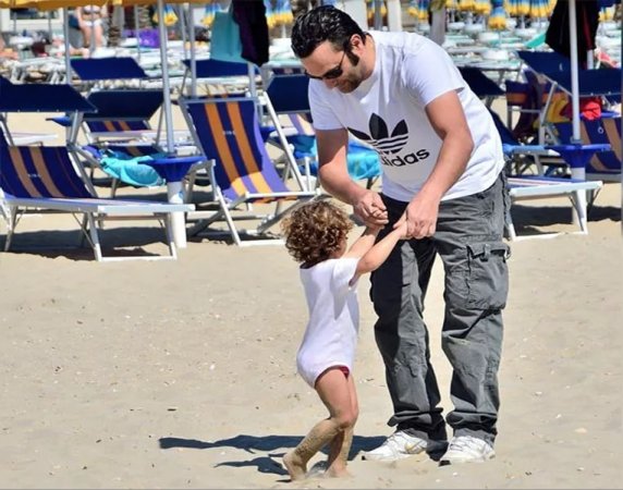 Un adulto gioca con un bambino sulla spiaggia vicino a lettini e ombrelloni.