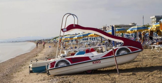 Un pedalò a forma di auto è arenato su una spiaggia con ombrelloni gialli e blu.