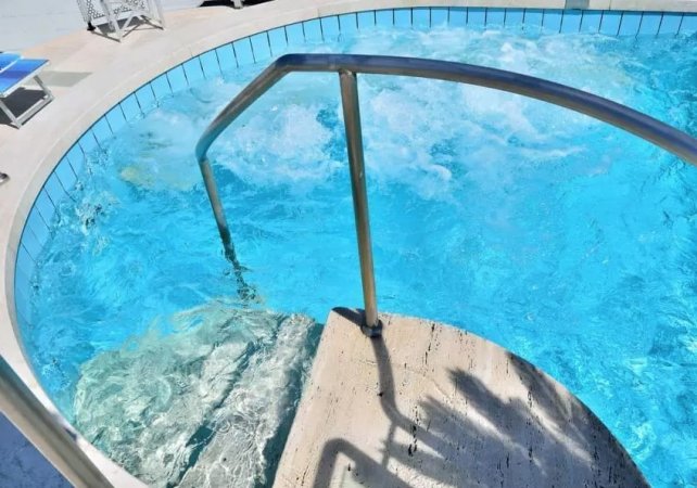 Piscina con gradini sommersi e acqua scintillante, ombreggiata dai bordi.