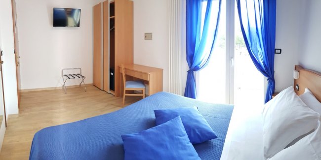 Camera con letto blu, scrivania e armadio, tenda blu e finestra aperta.