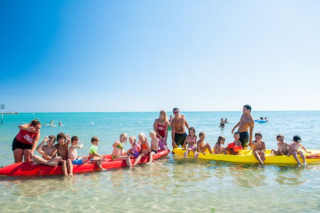 Gruppo di persone su pedalò in mare poco profondo con cielo sereno.