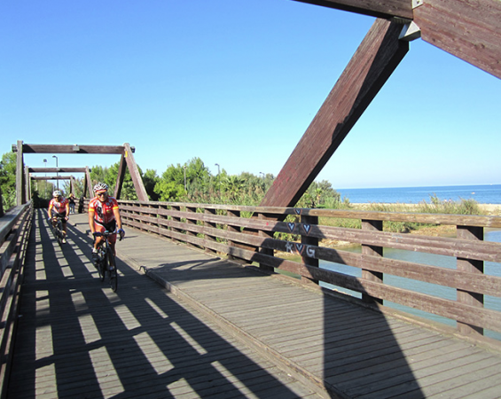 Ciclisti su un ponte di legno costiero con vista sul mare.