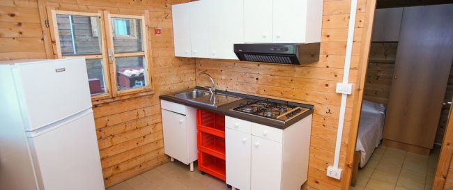 Cucina in legno con frigorifero bianco, fornello a gas e mobili bianchi.