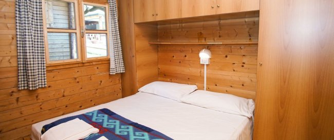 Camera da letto con pareti in legno, letto matrimoniale e finestra con tende a quadretti.