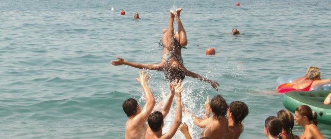 Persone in mare che lanciano una ragazza in aria durante un gioco in acqua.