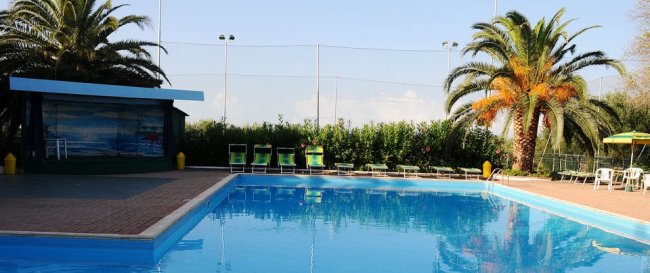 Piscina con palme e lettini verdi, cielo sereno.