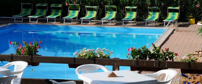 Piscina vuota con lettini verdi e fiori sul bordo.