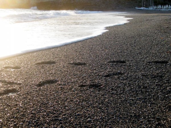 Impronte sulla spiaggia pietrosa con il mare al tramonto.