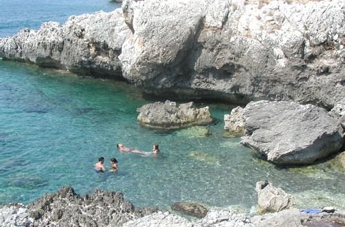Persone che nuotano in un mare roccioso e limpido.