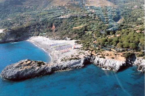 Spiaggia con ombrelloni colorati vista dall'alto, circondata da rocce e vegetazione.