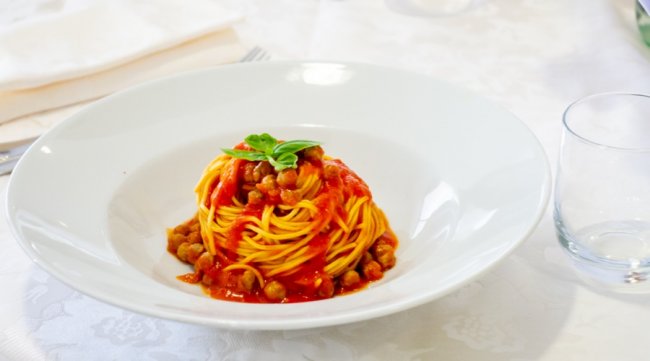 Un piatto di spaghetti con salsa di pomodoro, ceci e foglie di basilico fresco.