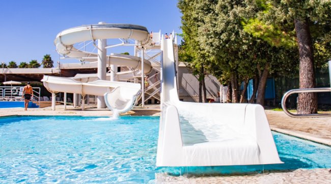 Scivolo d'acqua bianco presso una piscina all'aperto, sotto un cielo blu.