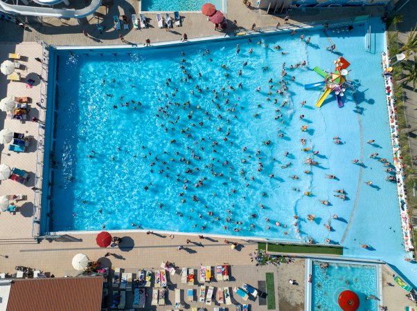 Piscina affollata vista dall'alto con scivoli d'acqua a sinistra e lettini intorno.
