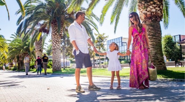 Famiglia che passeggia tra le palme, sorridendo.