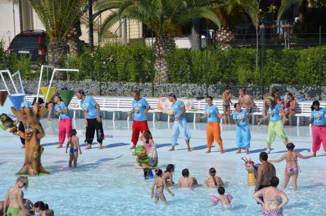 Persone in una piscina bassa si divertono, alcune partecipano a una lezione guidata.