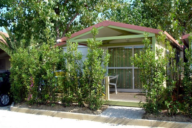 Bungalow con veranda avvolto da piante, vista frontale.