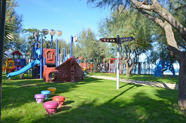 Parco giochi colorato su prato verde, con scivoli e strutture per arrampicarsi tra gli alberi.