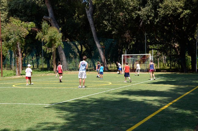 Un gruppo di persone gioca a calcio su un campo all'aperto circondato da alberi.