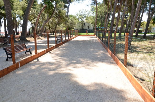 Un campo da bocce recintato tra alberi con panchine ai lati.
