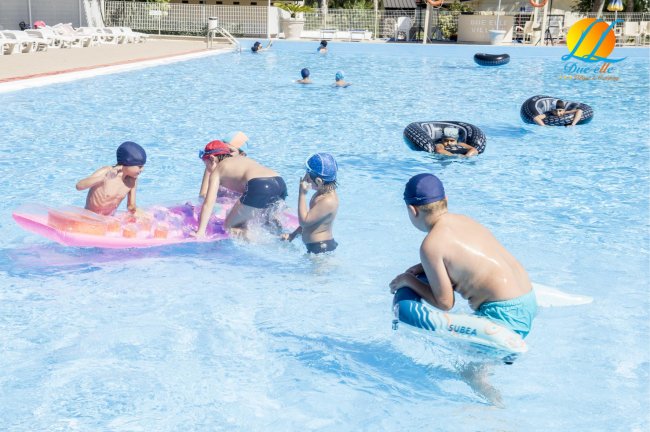 Bambini che giocano in piscina con materassini e ciambelle gonfiabili.