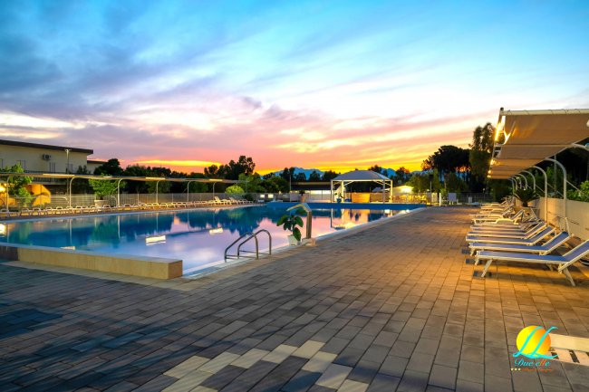 Piscina illuminata al tramonto con lettini disposti lungo il bordo.
