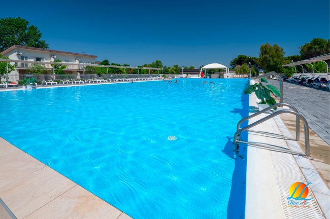 Ampia piscina con acqua azzurra, circondata da lettini bianchi.