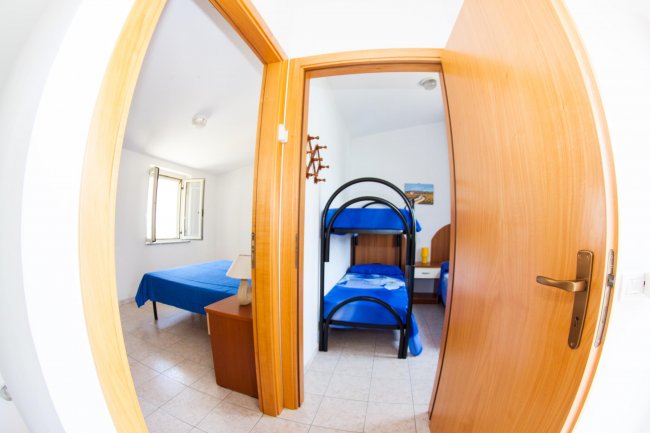 Due stanze con letti blu, una matrimoniale e una a castello, pavimento in piastrelle chiare.