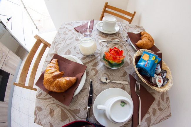 Tavolo apparecchiato per colazione con croissant, latte e biscotti.