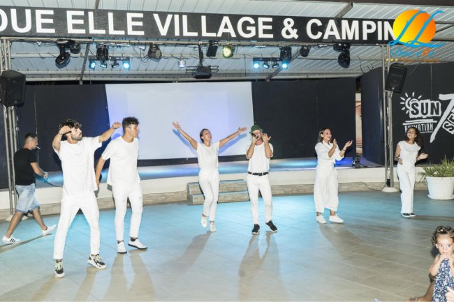 Persone sul palco che ballano, tutte vestite di bianco.