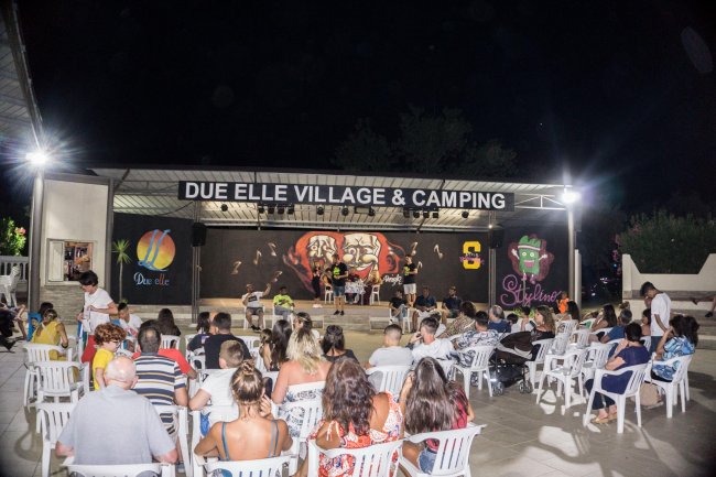 Spettacolo serale all'aperto in campeggio con pubblico seduto.