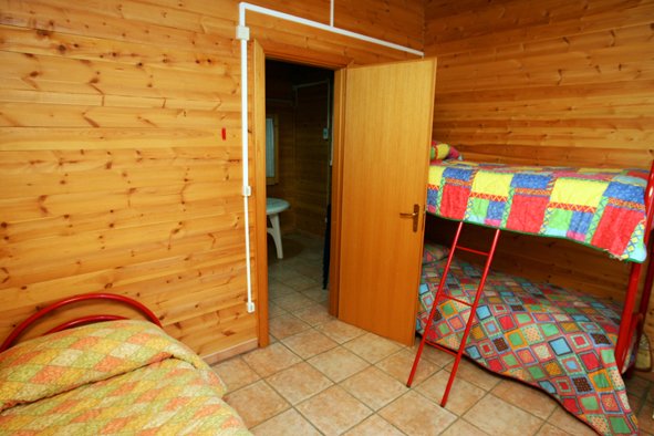 Camera con letti a castello, pareti di legno, porta aperta su un bagno.