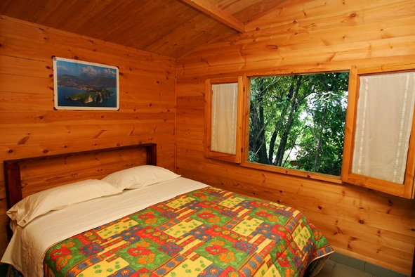 Camera con letto matrimoniale, coperta colorata e finestra vista alberi.