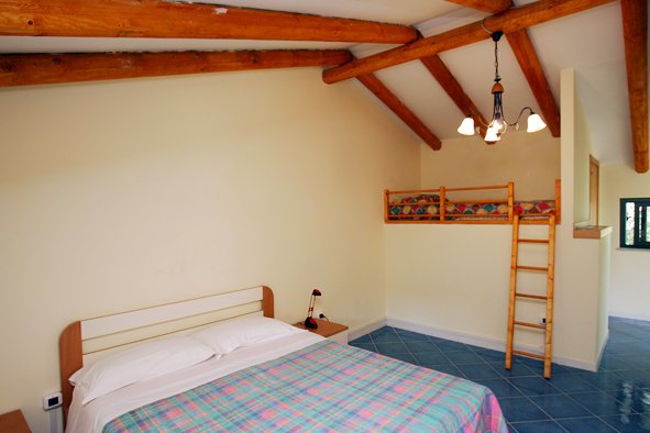 Camera con letto matrimoniale, travi a vista e letto a castello.