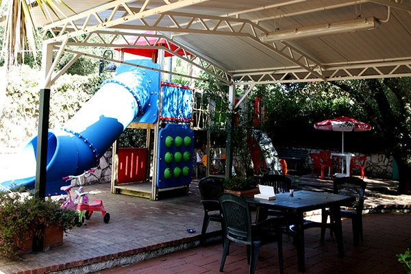 Area giochi coperta con scivolo blu e giochi per bambini su una terrazza.