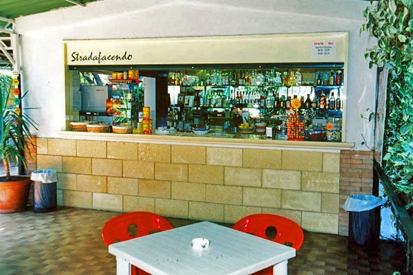 Un bar con sedie rosse e tavolo bianco all'aperto, circondato da piante.