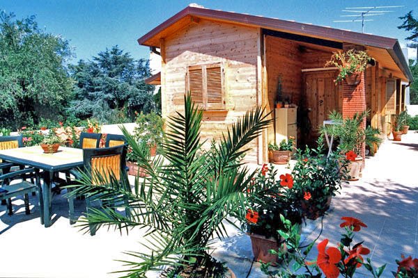 Una casetta di legno circondata da piante colorate e un'area con tavolo e sedie.
