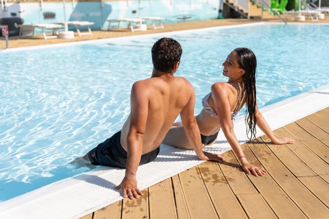 Due persone in costume da bagno sedute a bordo piscina.