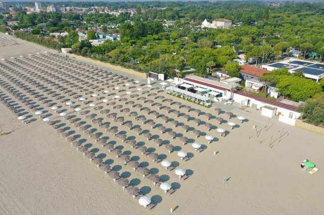 Spiaggia con file di ombrelloni e strutture verdi circostanti.