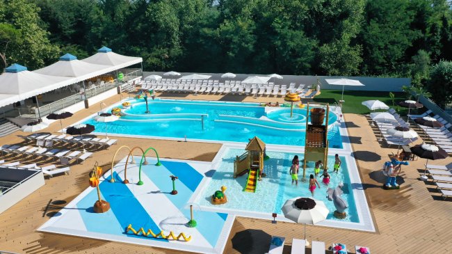 Una piscina con strutture per bambini e molte sdraio disposte intorno.