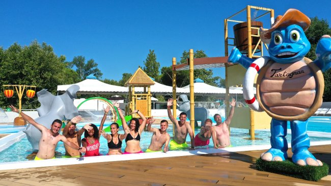 Persone sorridenti in una piscina accanto a una statua di tartaruga con salvagente.