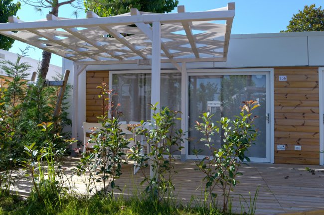 Bungalow con pergolato, circondato da piante e alberi.