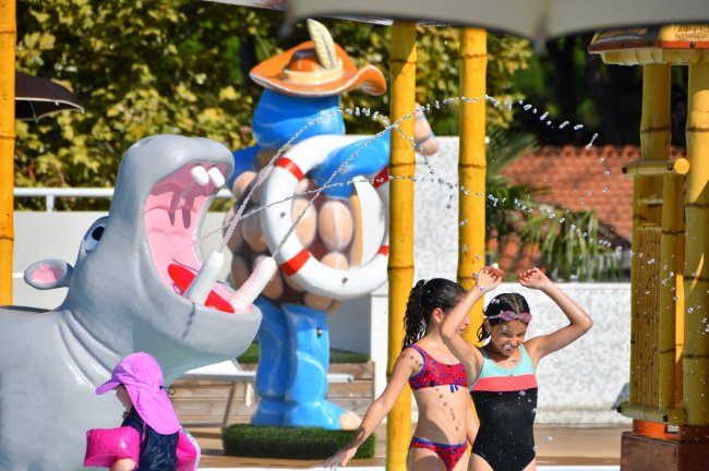 Bambini giocano con spruzzi d'acqua accanto a una statua di ippopotamo in un parco acquatico.