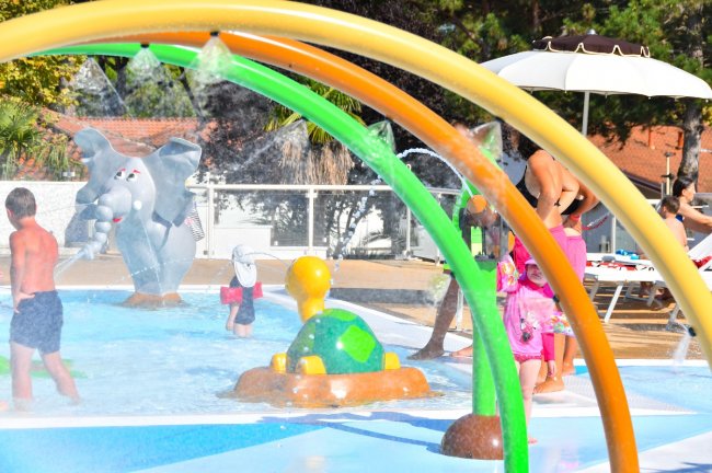 Bambini giocano in una piscina con scivoli e figure di animali colorati.