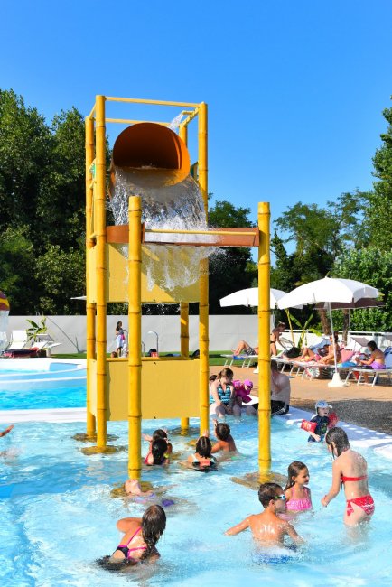 Bambini si divertono sotto un secchio gigante che versa acqua in piscina.