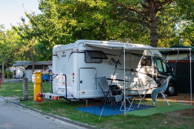 Camper bianco parcheggiato con sedie pieghevoli all'aperto.