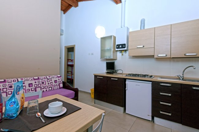 Cucina moderna con mobiletti chiari e scuri, tavolo apparecchiato e divano con cuscini colorati.