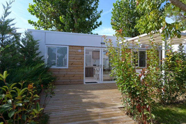 Un bungalow moderno circondato da alberi e piante con una veranda in legno.