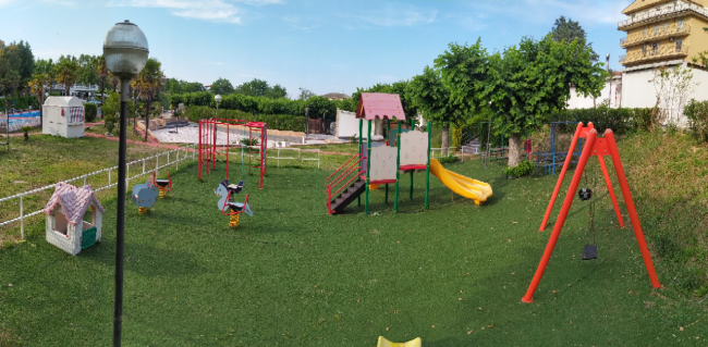 Parco giochi con altalene, scivolo e dondoli su prato verde.